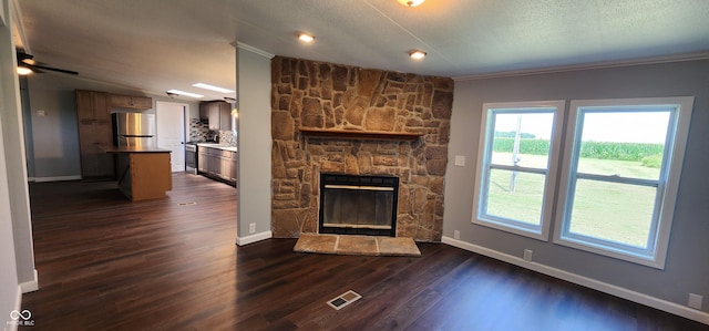 unfurnished living room featuring crown molding, a stone fireplace, dark wood-type flooring, and a textured ceiling