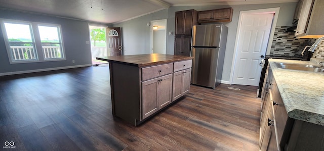 kitchen featuring dark wood-type flooring, lofted ceiling with beams, stainless steel fridge, a kitchen island, and backsplash