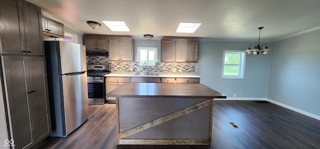 kitchen with sink, backsplash, hanging light fixtures, stainless steel appliances, and a kitchen island