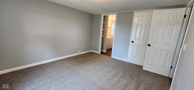 unfurnished bedroom with ensuite bath, a closet, and dark colored carpet