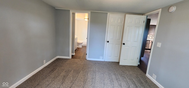 unfurnished bedroom with connected bathroom, a closet, and dark colored carpet