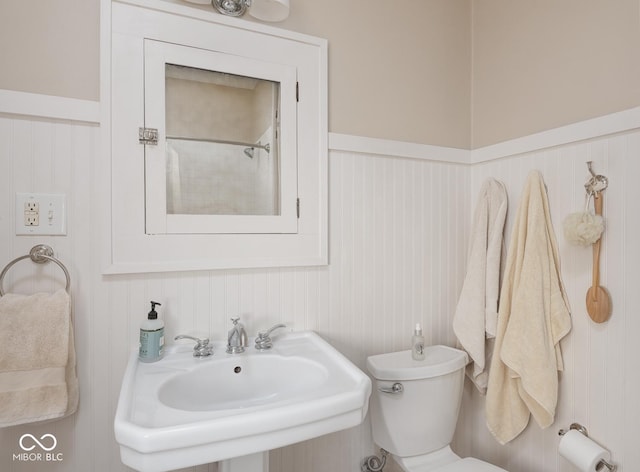 bathroom featuring a sink, a wainscoted wall, toilet, and walk in shower