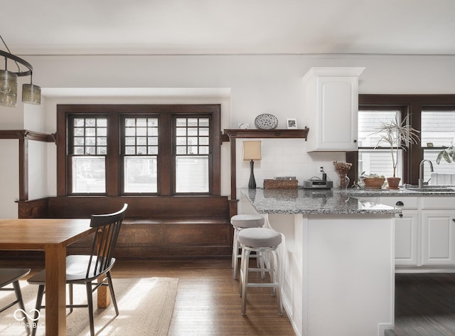 kitchen featuring wood finished floors, a breakfast bar, stone countertops, a sink, and white cabinets