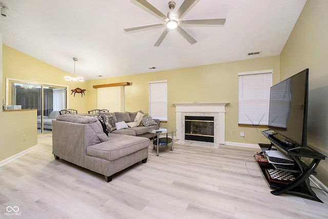 living room with a high end fireplace, vaulted ceiling, ceiling fan, and light wood-type flooring