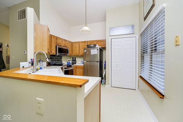 kitchen with sink, decorative light fixtures, appliances with stainless steel finishes, kitchen peninsula, and a high ceiling