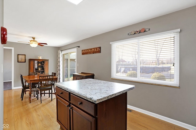 kitchen with ceiling fan, dark brown cabinetry, a center island, and light wood-type flooring