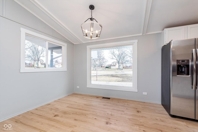 unfurnished dining area featuring light wood finished floors, baseboards, visible vents, lofted ceiling, and a notable chandelier