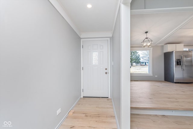 entryway featuring ornamental molding, light wood-type flooring, a chandelier, and baseboards