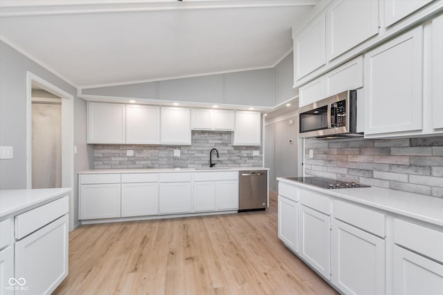 kitchen featuring stainless steel appliances, a sink, white cabinetry, vaulted ceiling, and light countertops