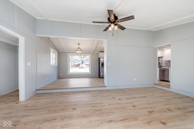 unfurnished living room featuring light wood-style floors, a decorative wall, and ceiling fan with notable chandelier