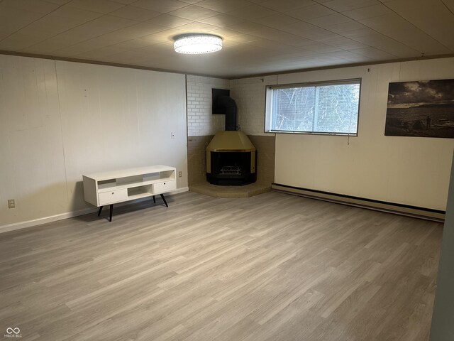 below grade area with baseboards, a wood stove, baseboard heating, and light wood-type flooring