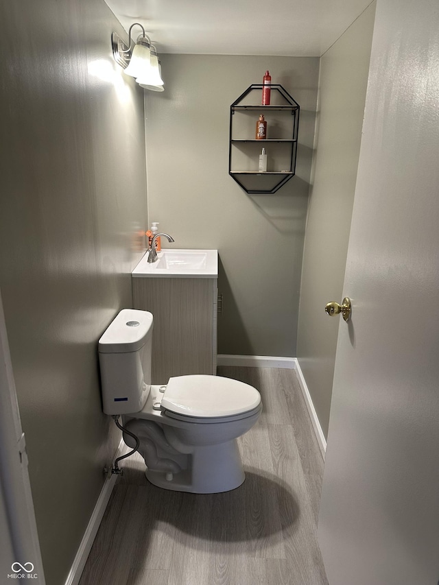 half bath featuring baseboards, wood finished floors, toilet, and vanity