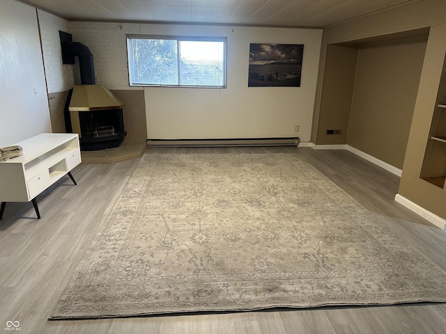 basement featuring baseboards, a wood stove, wood finished floors, and a baseboard heating unit