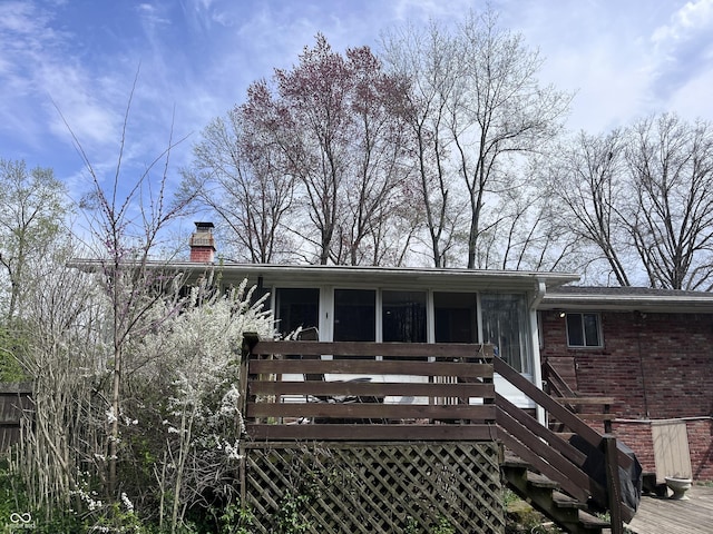 rear view of property with a chimney, brick siding, a wooden deck, and a sunroom