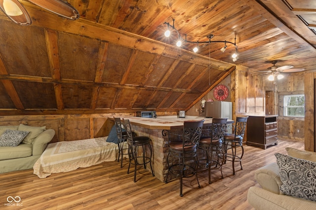interior space featuring wooden walls, lofted ceiling, bar, wood ceiling, and light hardwood / wood-style flooring