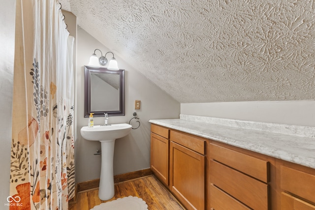 bathroom with vaulted ceiling, hardwood / wood-style floors, and a textured ceiling