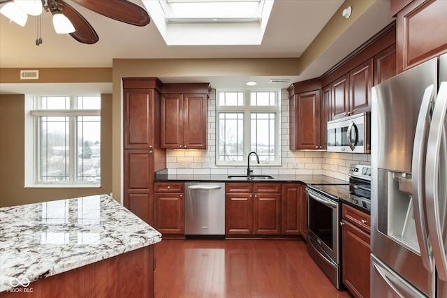 kitchen with stainless steel appliances, tasteful backsplash, visible vents, a sink, and dark stone countertops