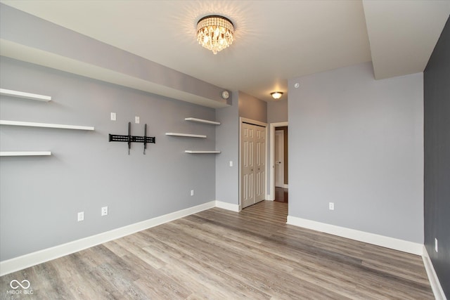 unfurnished room with an inviting chandelier, wood finished floors, and baseboards