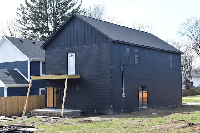 rear view of house with fence, board and batten siding, and a shingled roof