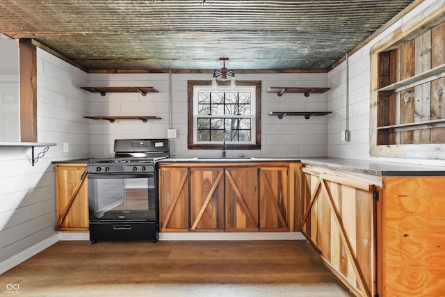 kitchen with sink, dark wood-type flooring, wood walls, and black gas range