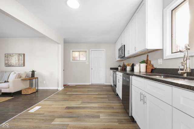 kitchen featuring sink, white cabinetry, appliances with stainless steel finishes, dark stone counters, and light hardwood / wood-style floors