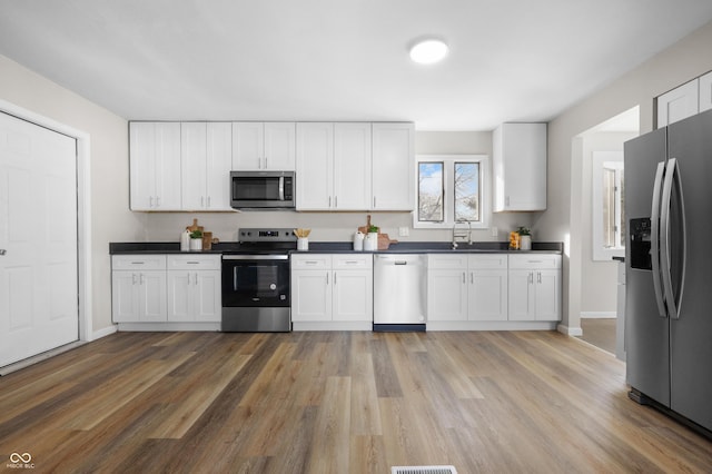 kitchen with sink, wood-type flooring, stainless steel appliances, and white cabinets