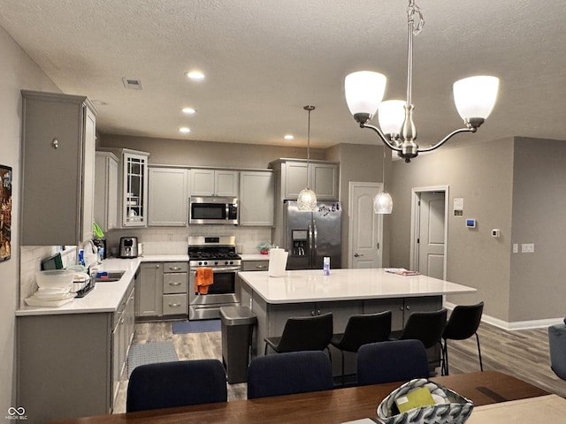 kitchen with a breakfast bar area, appliances with stainless steel finishes, gray cabinetry, a kitchen island, and decorative light fixtures