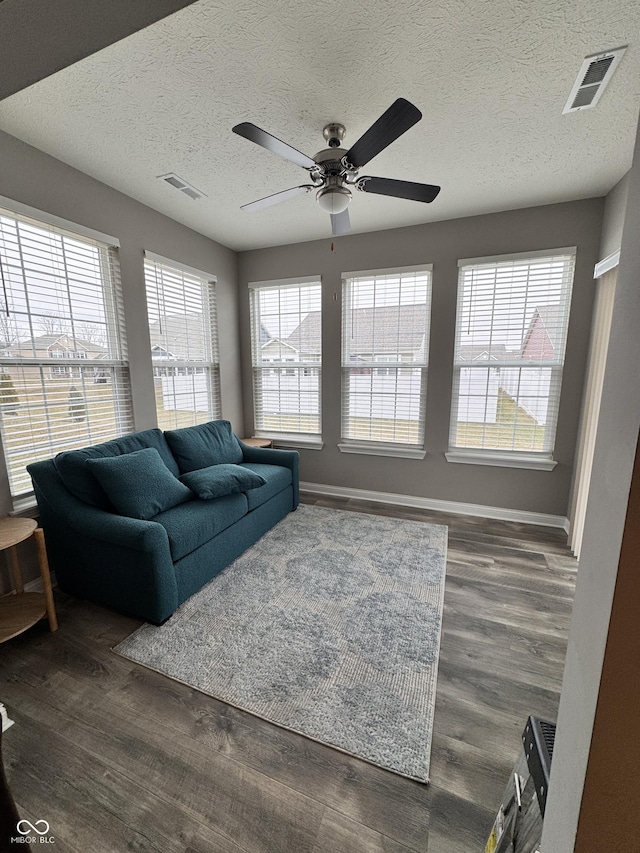 living room with dark wood-type flooring, ceiling fan, and a textured ceiling