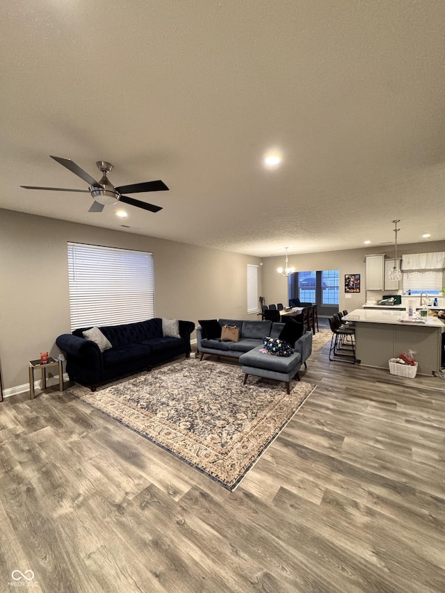 living room featuring hardwood / wood-style flooring, ceiling fan with notable chandelier, and a textured ceiling