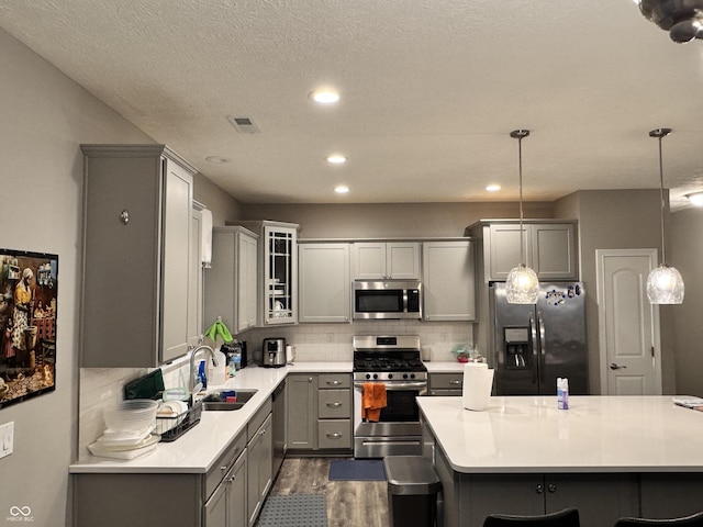 kitchen featuring stainless steel appliances, hanging light fixtures, gray cabinets, and sink