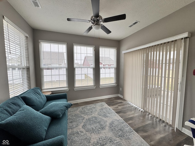 living area featuring dark wood-type flooring, ceiling fan, a textured ceiling, and a wealth of natural light