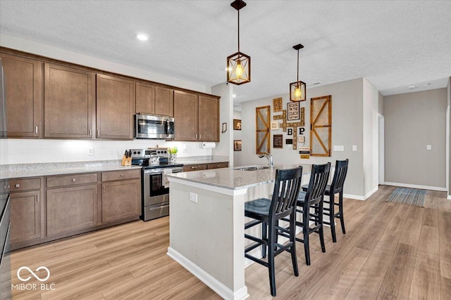 kitchen featuring decorative light fixtures, a center island with sink, appliances with stainless steel finishes, a sink, and light stone countertops