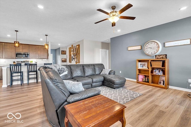 living room with ceiling fan, light wood finished floors, a textured ceiling, and baseboards