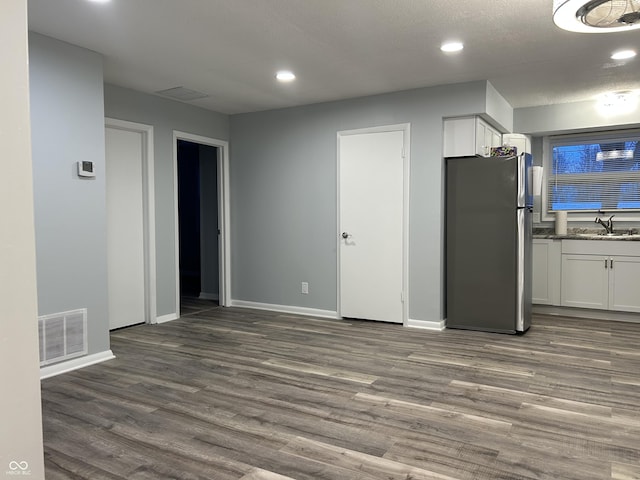 kitchen with stainless steel refrigerator, white cabinetry, sink, dark stone counters, and dark wood-type flooring