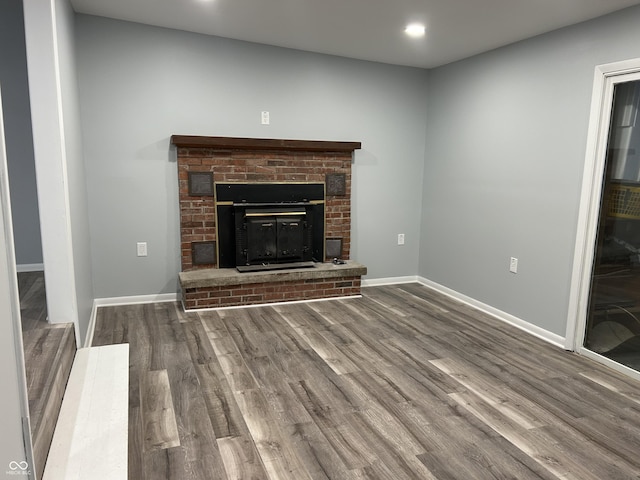 unfurnished living room with wood-type flooring and a brick fireplace