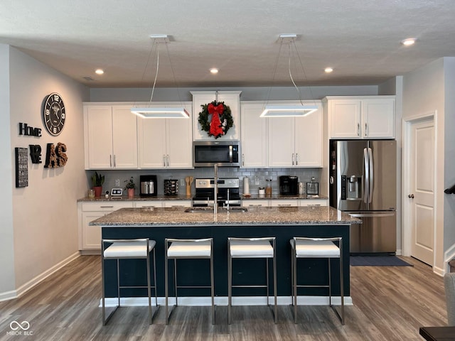 kitchen with stainless steel appliances, an island with sink, a kitchen bar, and white cabinets