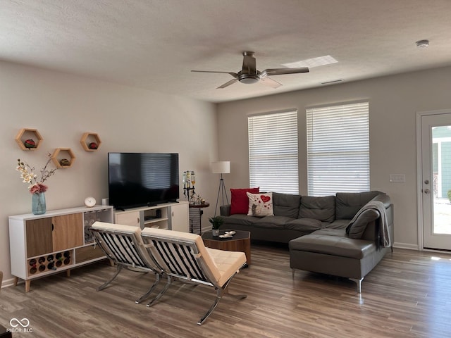 living room featuring ceiling fan, a textured ceiling, baseboards, and wood finished floors