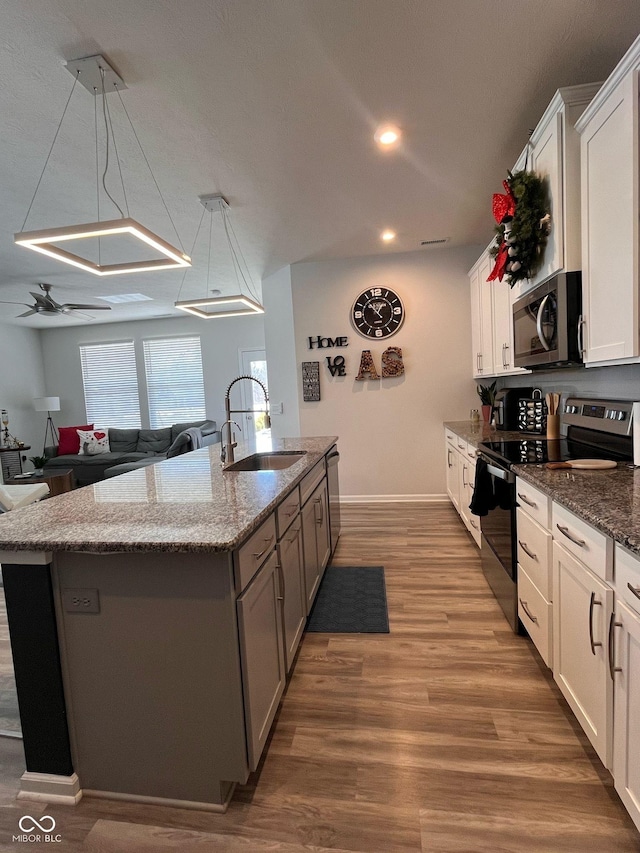 kitchen with stainless steel appliances, white cabinetry, a sink, an island with sink, and wood finished floors