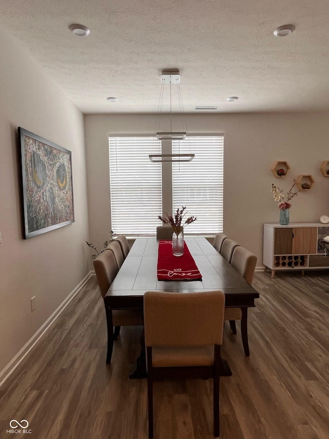 dining space with visible vents, a textured ceiling, baseboards, and wood finished floors