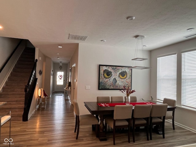 dining room featuring stairway, a textured ceiling, visible vents, and wood finished floors