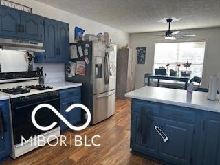 kitchen with blue cabinetry, white range with gas stovetop, stainless steel fridge, dark hardwood / wood-style flooring, and ceiling fan