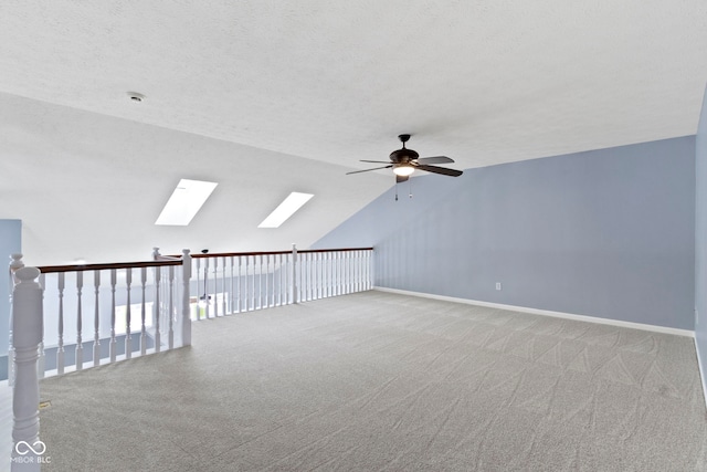 additional living space with ceiling fan, lofted ceiling with skylight, light carpet, and a textured ceiling