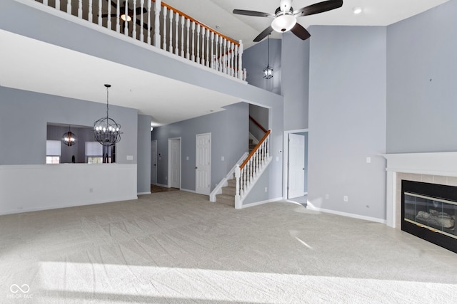 unfurnished living room with ceiling fan with notable chandelier, a tile fireplace, a towering ceiling, and carpet flooring