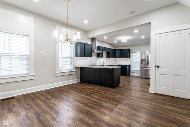 kitchen with stainless steel refrigerator with ice dispenser, blue cabinets, a breakfast bar area, dark hardwood / wood-style floors, and wall chimney range hood