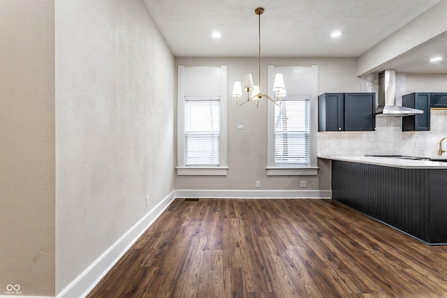 kitchen featuring tasteful backsplash, hanging light fixtures, dark wood-type flooring, an inviting chandelier, and wall chimney exhaust hood