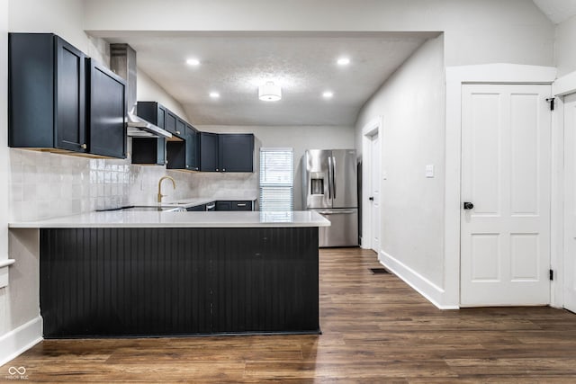 kitchen featuring a kitchen bar, dark hardwood / wood-style flooring, stainless steel fridge, kitchen peninsula, and backsplash