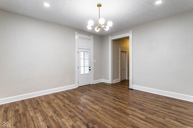 empty room featuring dark wood-type flooring, a textured ceiling, and an inviting chandelier