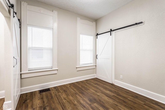 spare room featuring a barn door, dark wood-type flooring, and a textured ceiling