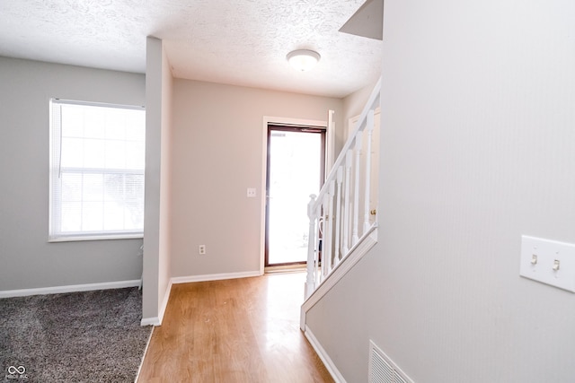 entrance foyer with a textured ceiling, visible vents, baseboards, stairway, and light wood finished floors