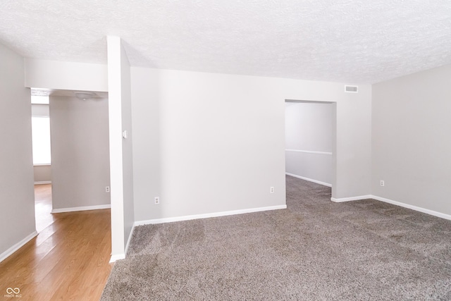 spare room with baseboards, visible vents, a textured ceiling, and wood finished floors